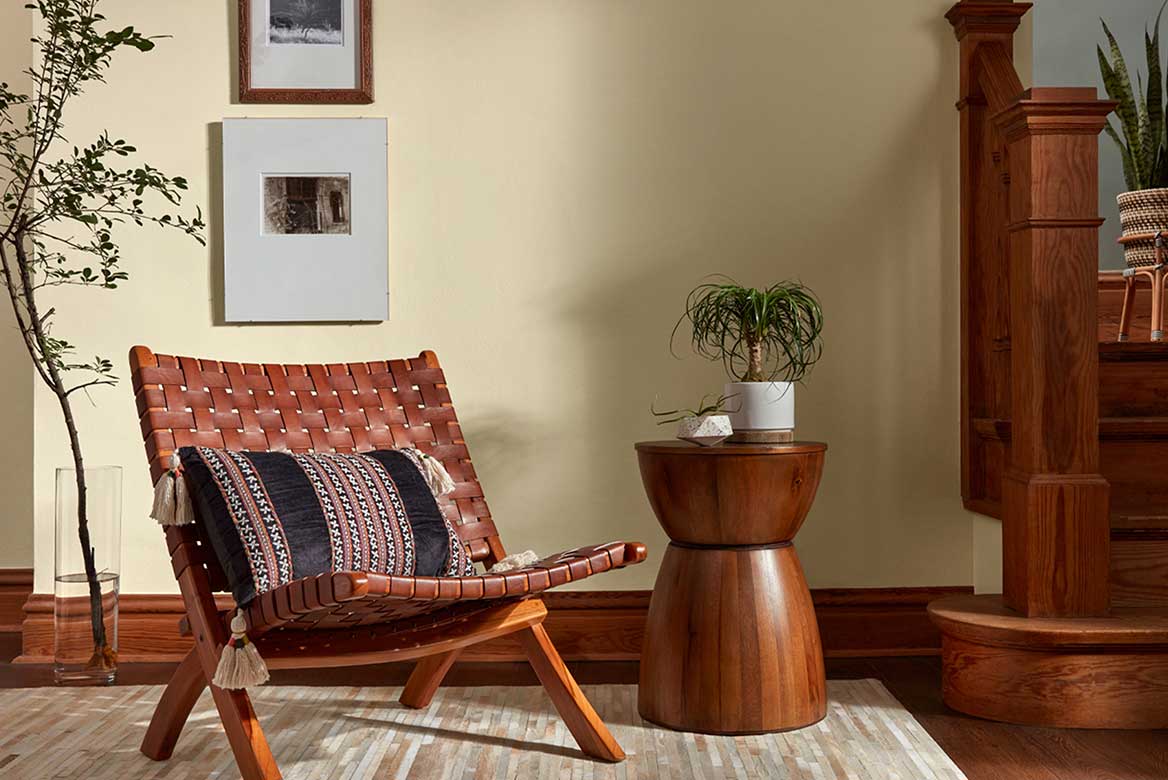 Warm white walls with woven leather chair, curved wood table sitting next to staircase with heavy wood handrail.