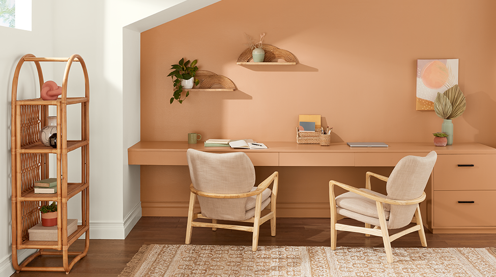 Room with a desk, two chairs, plants, art on a shelf and a bamboo-style bookcase.